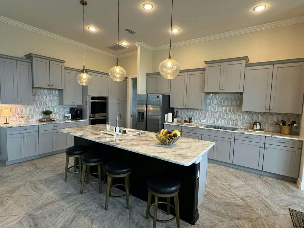 Contemporary Kitchen with White and Gray Marble Countertops, Island with Four Barstools, Light Gray Cabinets, and White and Gold Picket Tile Backsplash